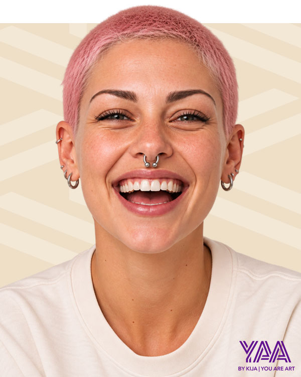 YAA Piercing campaign portrait of a smiling woman with short pink hair and facial piercings